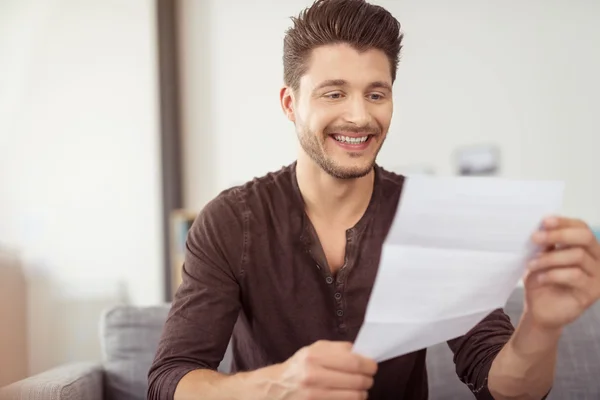 Joyeux beau garçon lisant une lettre au canapé — Photo