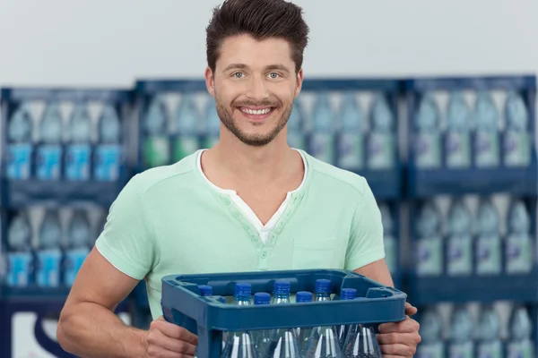 Jeune homme souriant portant une caisse d'eau embouteillée — Photo