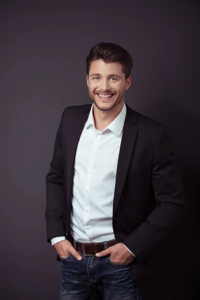 Guapo joven sonriendo a la cámara contra Gray — Foto de Stock