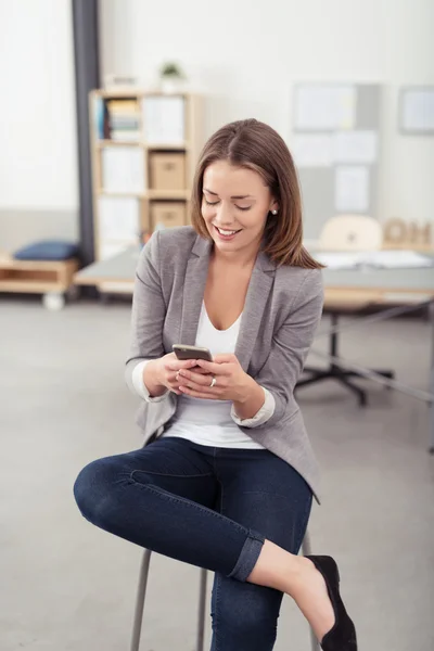 Glückliche Bürofrau auf einem Schemel mit Telefon beschäftigt — Stockfoto