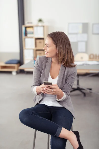 Leende Office kvinna på en pall som håller telefonen — Stockfoto