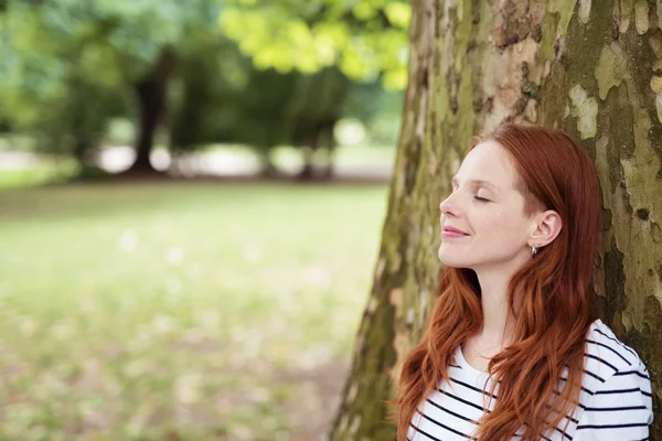 Feliz chica rubia pensativa apoyada contra el árbol — Foto de Stock