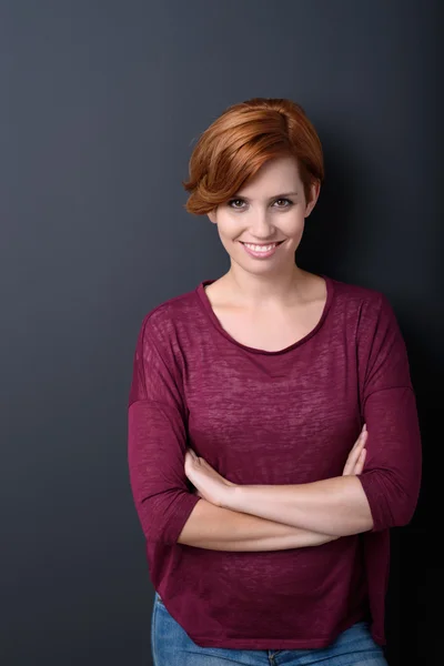 Femme souriante avec les bras croisés contre gris — Photo