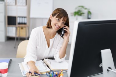Happy Businesswoman at her Desk Talking on Phone clipart