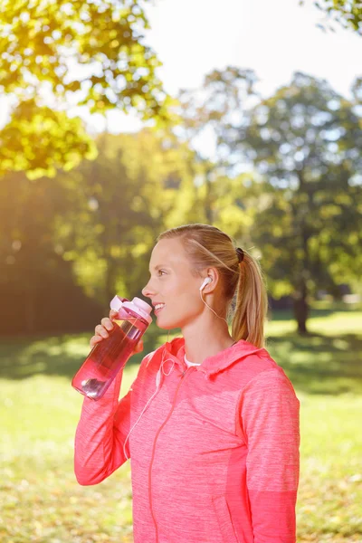 Женщина пьет воду после тренировки в парке — стоковое фото