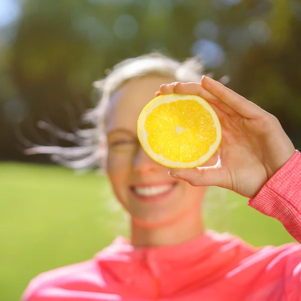 Jovencita juguetona sosteniendo una naranja en su ojo — Foto de Stock