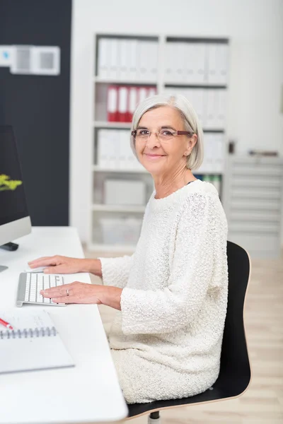 Senior Businesswoman en su escritorio sonríe en cámara —  Fotos de Stock