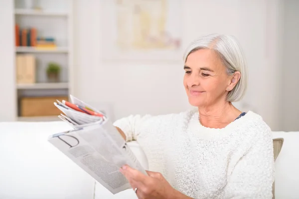Счастливая старшая леди читает журнал на диване — стоковое фото