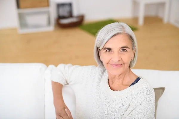 Μέσης ηλικίας γυναίκα στο το καναπέ χαμογελώντας σε κάμερα — Φωτογραφία Αρχείου