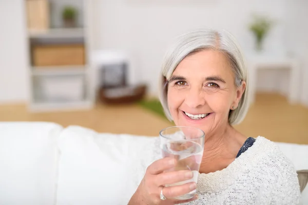 Starší žena v gauči, drží sklenici vody — Stock fotografie
