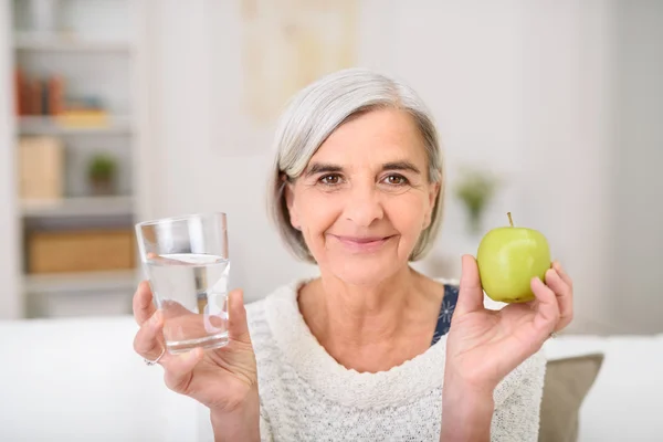 Mujer mayor sosteniendo vaso de agua y manzana — Foto de Stock