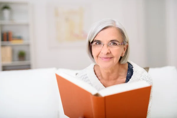 Femme âgée tenant un livre, souriant à la caméra — Photo