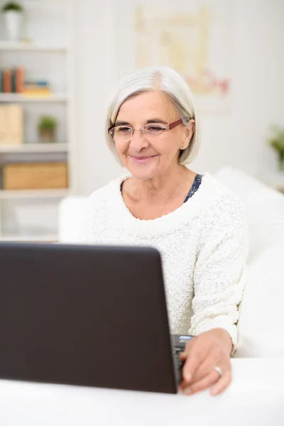 Счастливая пожилая женщина с ноутбуком в гостиной — стоковое фото