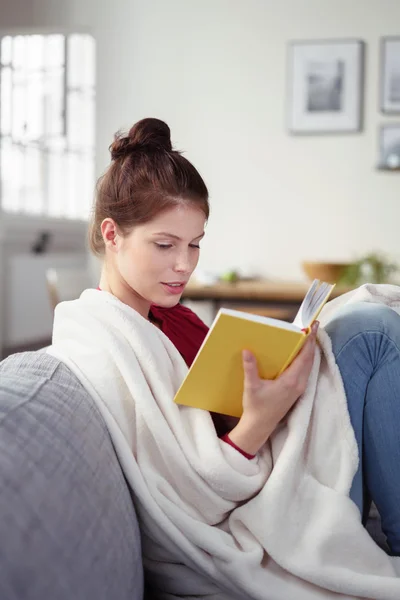 Mujer relajándose en el sofá con un libro — Foto de Stock