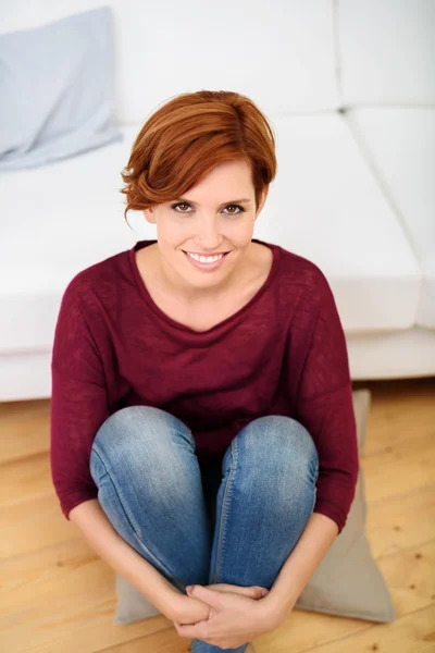 Lachende vrouw die zit op het hoofdkussen op de verdieping — Stockfoto