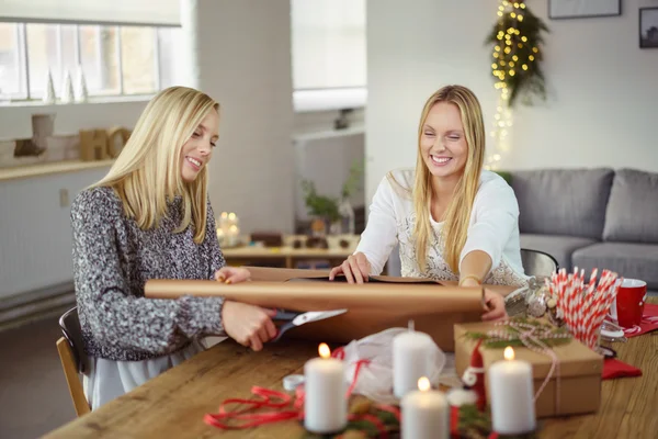 Zwei Schwestern lächeln, während sie Weihnachtsgeschenke einpacken — Stockfoto