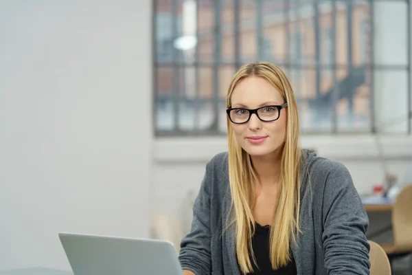 Bürofrau sitzt an ihrem Schreibtisch und lächelt in die Kamera — Stockfoto