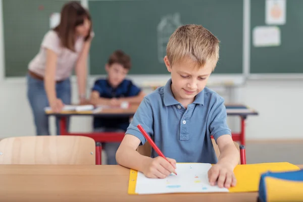 Young boy sitting writing notes at school — ストック写真