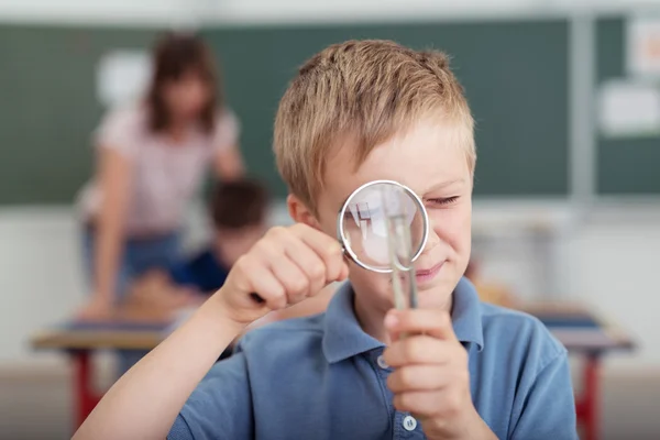 Мальчик использует увеличительное стекло в классе — стоковое фото