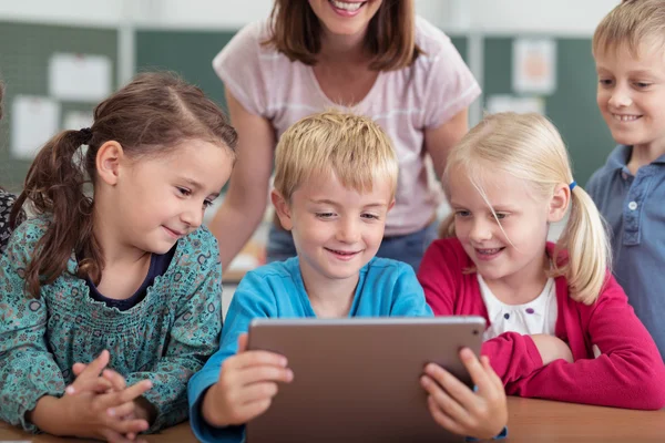 Crianças em idade escolar sorrindo olhando para um tablet — Fotografia de Stock