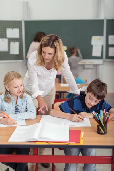 Lärare att hjälpa två unga skolbarn — Stockfoto