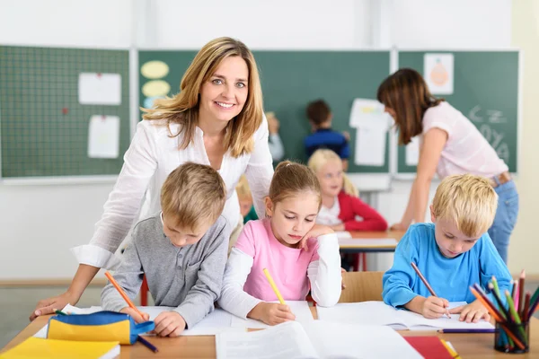 Lärare ler mot kameran samtidigt hjälpa barnen — Stockfoto