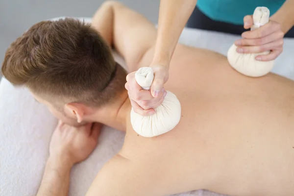 Junger Mann genießt eine Massage mit Kräuterkompressen — Stockfoto