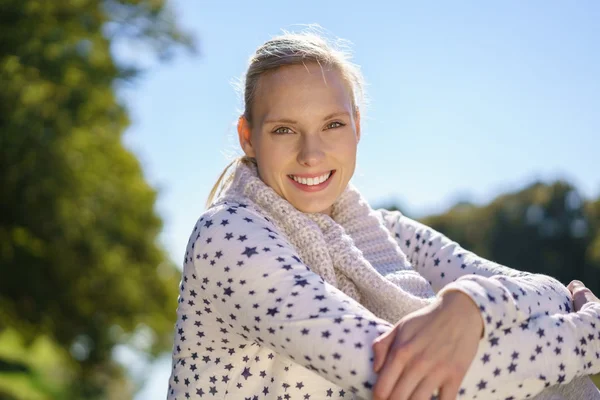 Lächelnde junge Frau sitzt draußen — Stockfoto