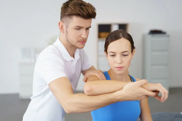 Joven fisioterapeuta profesional masculino examinando el brazo de una paciente femenina — Foto de Stock