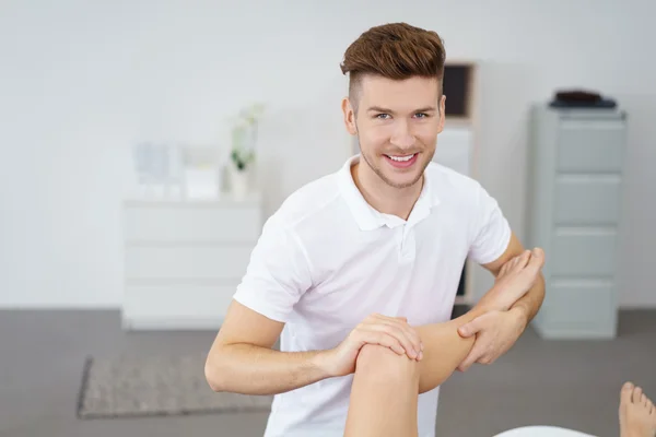 Joven fisioterapeuta masculino profesional examinando la rodilla lesionada de un paciente —  Fotos de Stock