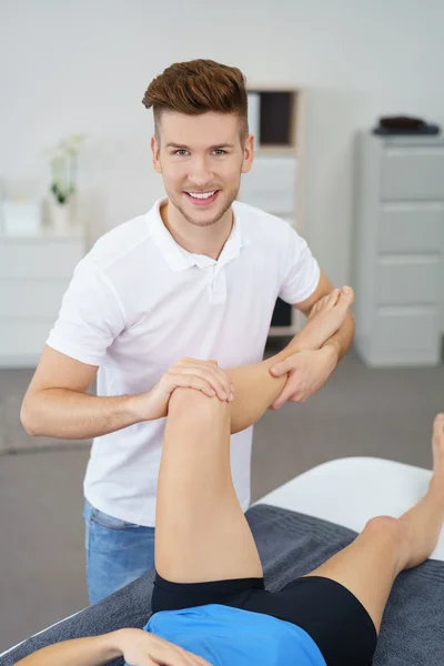 Glimlachend mannelijke fysiotherapeut onderzoeken de gewonde knie van een vrouwelijke patiënt — Stockfoto