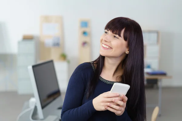 Glückliche Studentin lehnt an ihrem Schreibtisch, während sie ihr Handy benutzt — Stockfoto