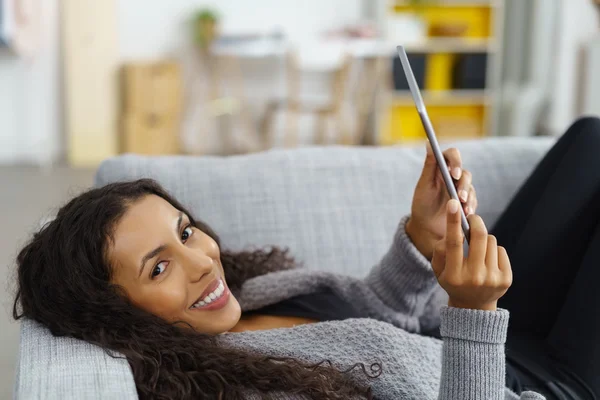 Smiling woman lying on the sofa using tablet — 스톡 사진