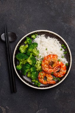 Siyah tabakta teriyaki karides, pirinç ve brokoli. Asyalı sağlıklı yiyecekler. Süslü deniz ürünleri. Üst görünüm