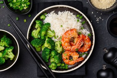 Siyah tabakta teriyaki karides, pirinç ve brokoli. Asyalı sağlıklı yiyecekler. Süslü deniz ürünleri. Üst görünüm