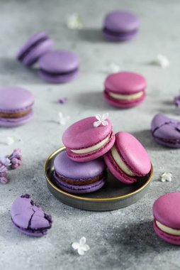 Eflatun çiçeklerle süslenmiş metal bir plaka üzerinde pembe ve mor badem kurabiyeleri. Üç badem kurabiyesi yaklaş. Seçici odak