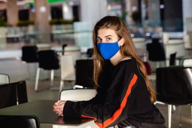 Yemek reyonunun arka planındaki genç bir kız Coronavirus hastalığının yayılmasını önleyen mavi bir maske takıyor. Yüzünde cerrahi maske olan genç bir kadının SARS-cov-2 'ye yakın çekimi.