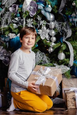 Gülümseyen çocuk Noel ağacının yanında elinde Noel hediyesi tutuyor. Noel konsepti.