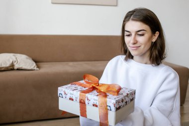 Güzel, genç, gülümseyen bir kadın, Noel hediyesi kutusunu portakal rengi kurdeleyle evde tutuyor. Yeni yıl kavramı, Noel