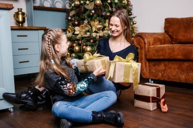 Anne, Noel ağacının yakınındaki kızına sürpriz yapacak. Mutlu gülümseyen kız annesinden hediye alır..