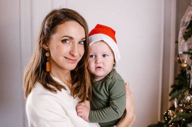 Noel Baba şapkalı mutlu anne ve sevimli bebek Noel 'i kutluyor. Yeni yıl tatili. Anne oğlanla oynuyor..