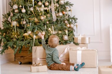 Noel ağacının altında hediye kutusuyla oturan şirin küçük çocuk. Noel ve yeni yıl tatili konsepti.