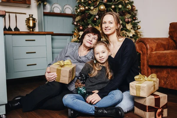 Kid with mom and grandmother are sitting hugging on against a Christmas tree. Christmas mood. Portrait loving family. Merry Christmas and Happy Holidays!