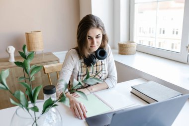 İnternet sohbet öğretmeniyle kulaklık takan çekici bir kız sınava hazırlanıyor, kız öğrenci internetten öğreniyor, dizüstü bilgisayara bakarak Webinar izliyor, uzaktan eğitim alıyor..