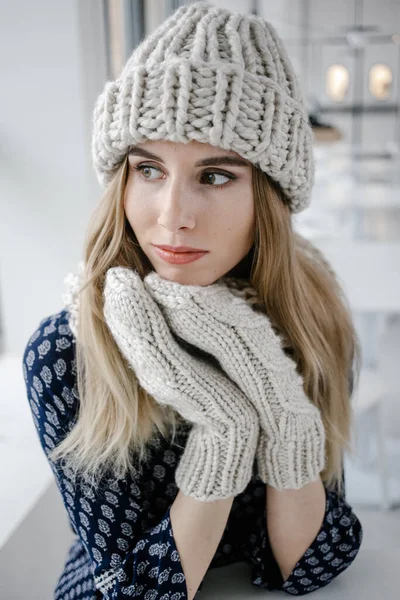 Beautiful cute woman wearing knitted winter hat and mittens on cafe background.