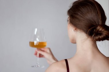 Arkaya bakan genç bir kadın elinde bir bardak beyaz şarap tutuyor ve tadıyor. Kıza odaklan. Boşluğu kopyala