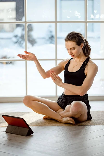 Yoga teacher conducting virtual yoga class at home on a video conference. Beautiful fit woman practicing online yoga with tablet. Home fitness and workout concept. Online training