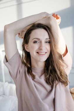 Mutlu, genç, güzel bir kadın ellerini kaldırır, yatak odasındaki yatağın yanında durur. İnsanlar ve Sabah konsepti.