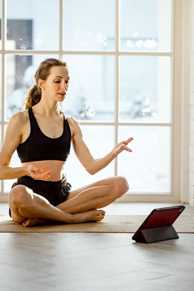 Yoga teacher conducting virtual yoga class at home on a video conference. Beautiful fit woman practicing online yoga with tablet. Home fitness and workout concept. Online training