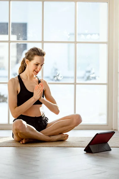 Yoga teacher conducting virtual yoga class at home on a video conference. Beautiful fit woman practicing online yoga with tablet. Home fitness and workout concept. Online training